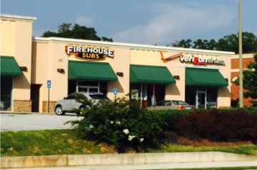 Strip mall storefronts with Firehouse Subs and Verizon Wireless signs, parked cars, and green awnings