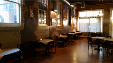 Warmly lit empty cafe with wooden tables, chairs, and large windows by the wall.