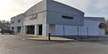 Verizon storefront in a large white building with an empty parking lot under a clear sky