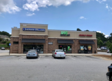 Strip mall storefronts with parked cars under a blue sky