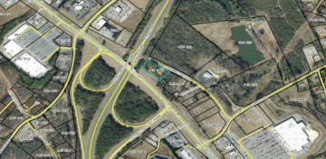 Aerial view of a highway interchange with roads, buildings, and green spaces in a suburban area.