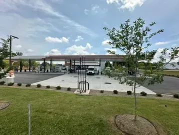 Modern gas station with covered pumps, parking lot, and grassy foreground under a cloudy sky