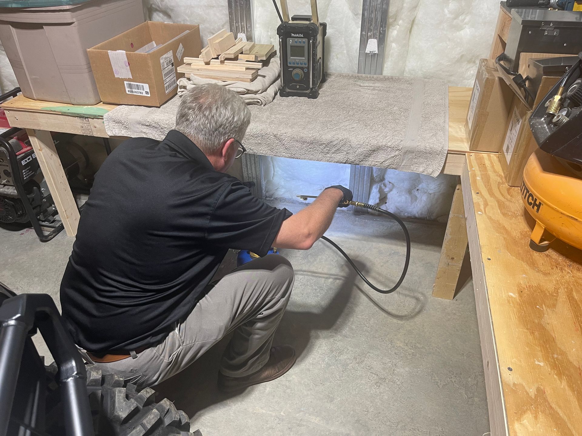 A man is kneeling down in a garage spraying for insects