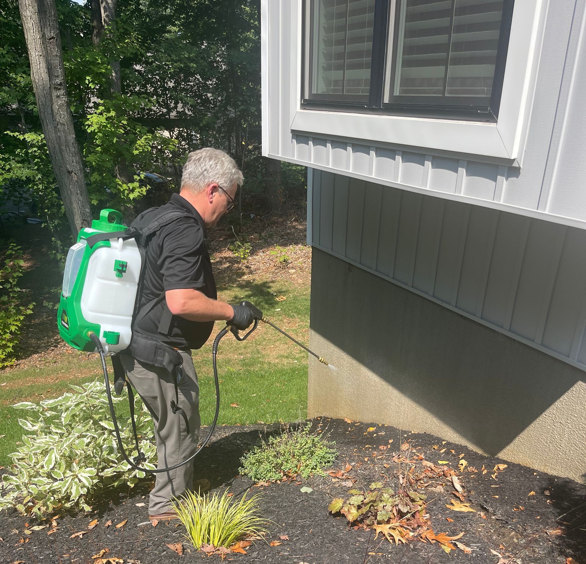 A man is spraying a house with a backpack sprayer for pest control.