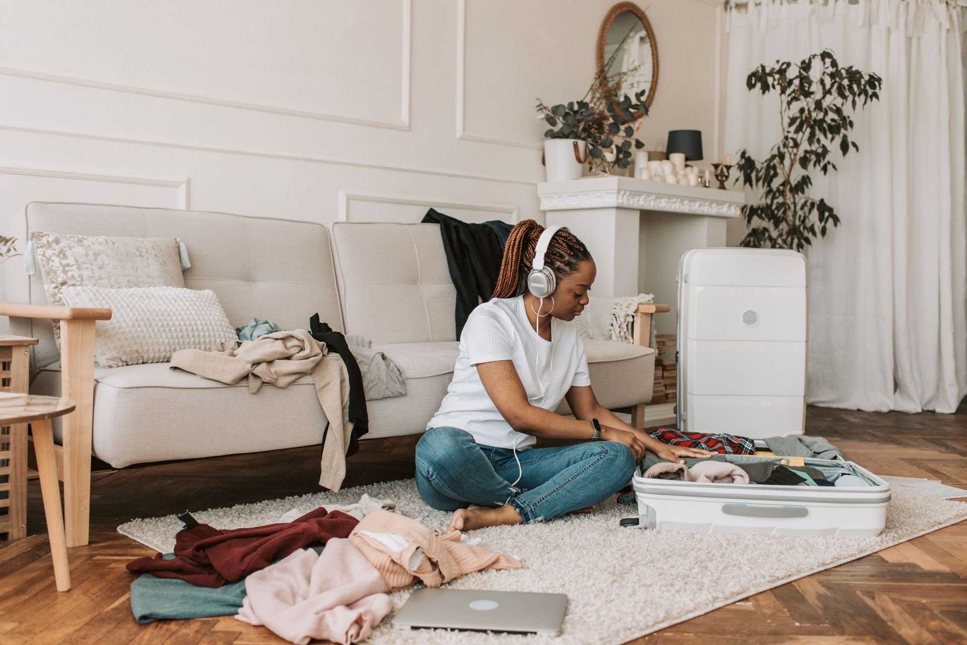 Woman sitting on a living room rug, packing items into an open suitcase beside a couch.