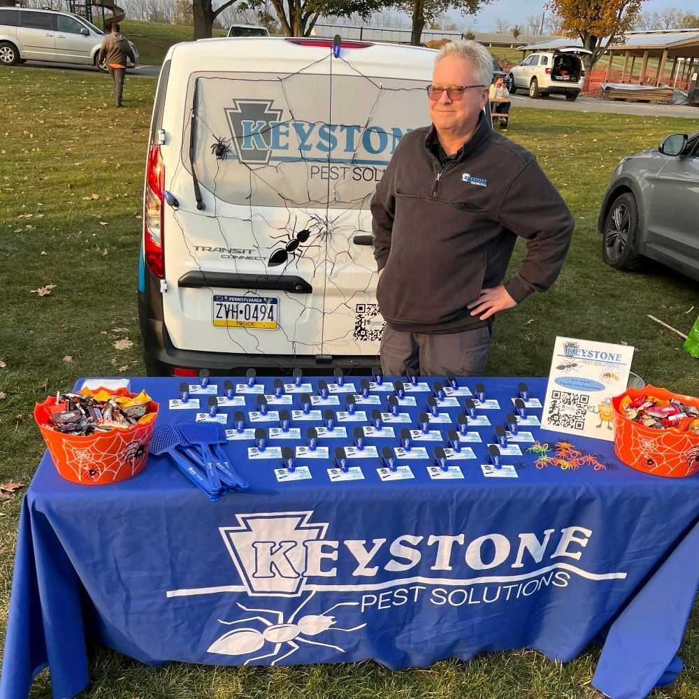 A man stands in front of a keystone pest solutions table at a halloween event