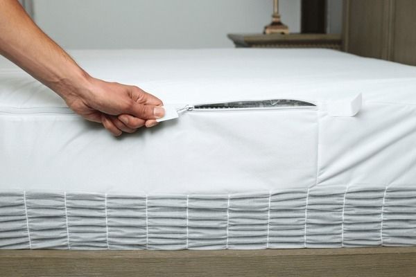 A person is putting a white mattress protector on a bed.