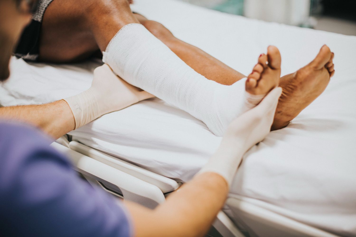 Person wrapping a patient’s lower leg in a white bandage on a hospital bed