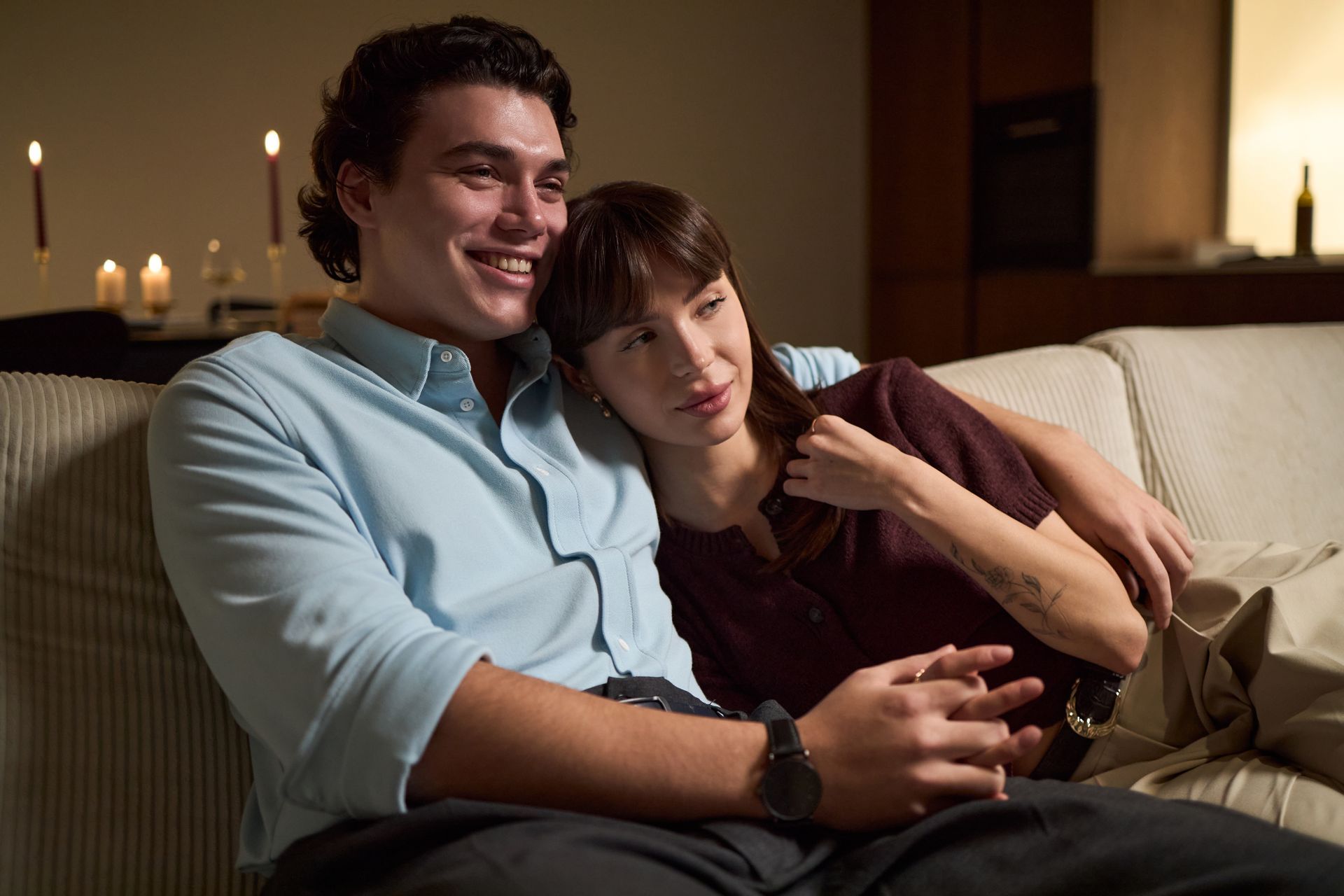 Couple relaxing on a couch, smiling and cuddling in a warmly lit living room.