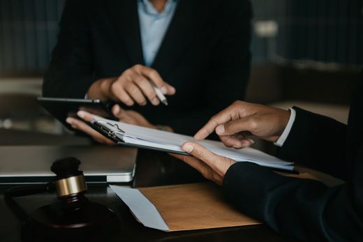 Businesspeople exchanging documents at a desk with a gavel and clipboard