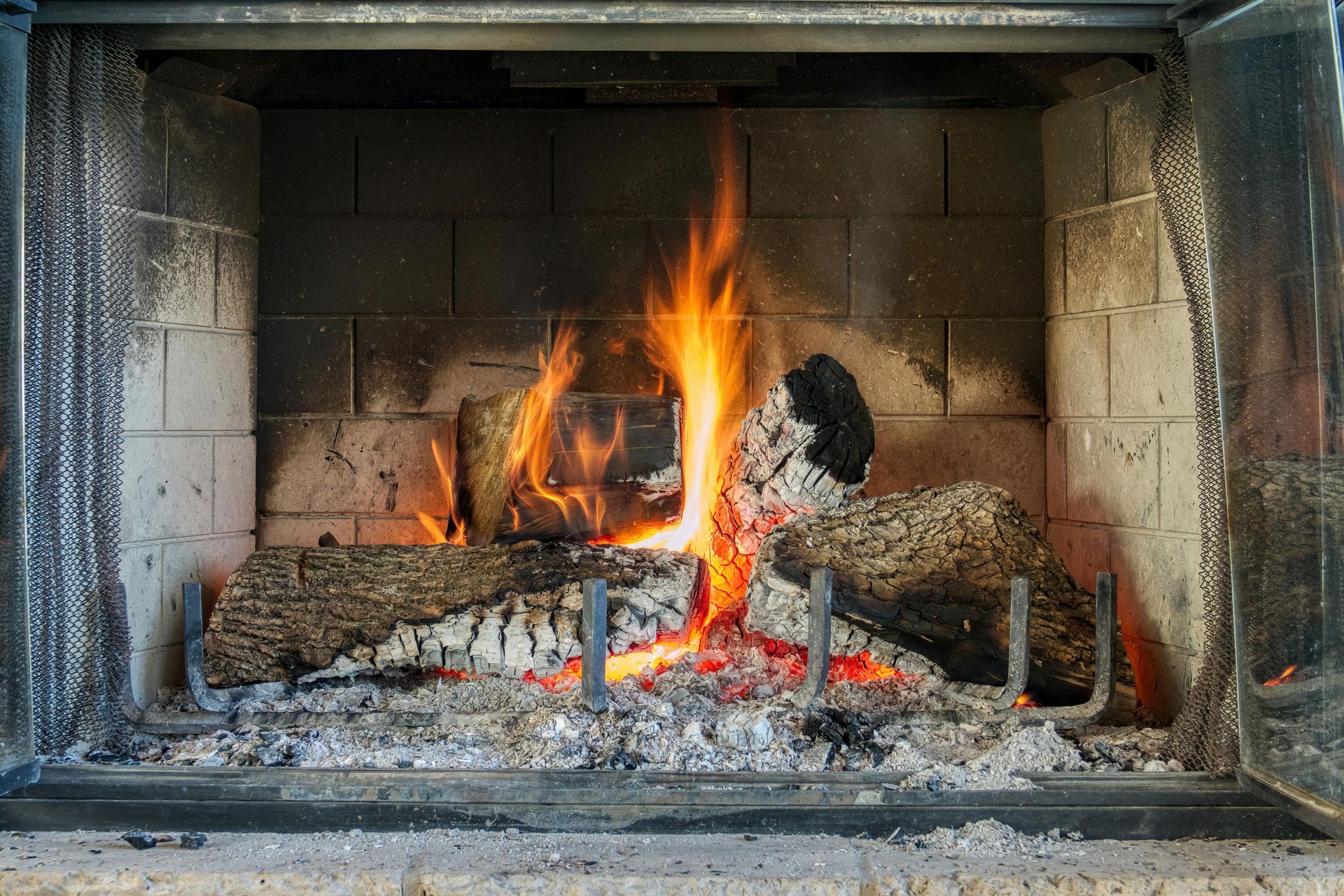 Burning logs and embers inside a stone fireplace with bright flames
