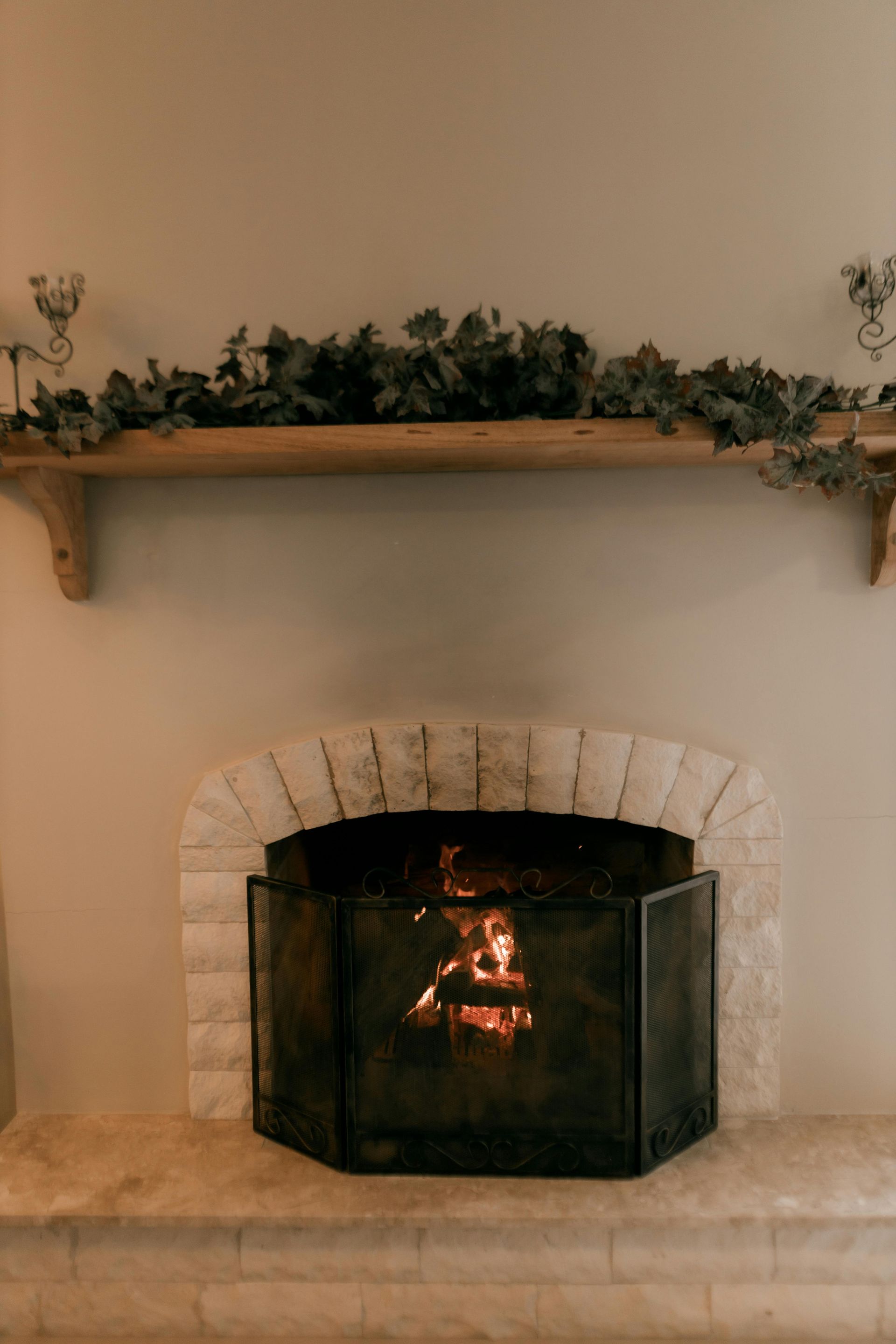 Brick fireplace with a small fire burning, topped by a wooden mantel with greenery.