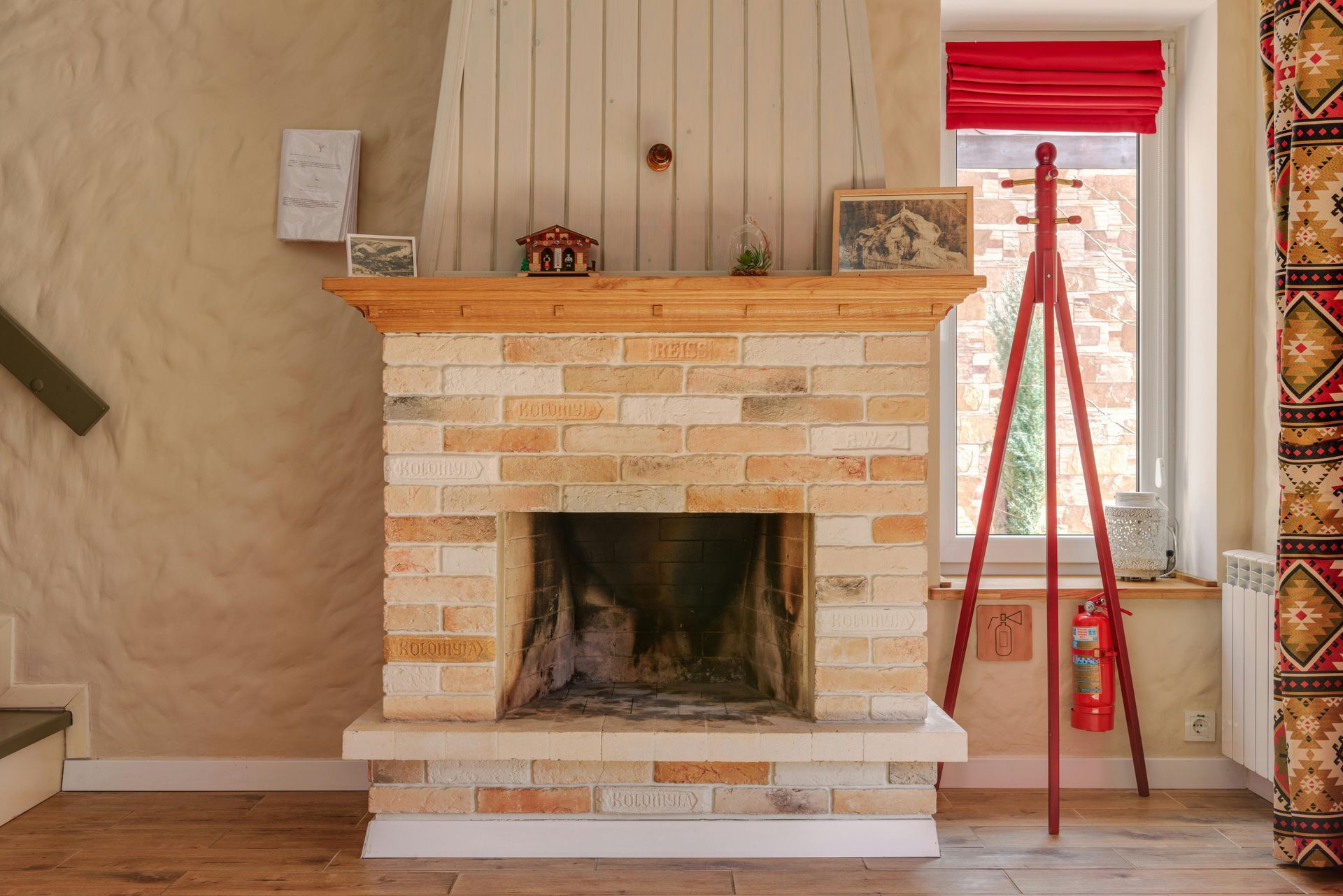 Brick fireplace with wooden mantel in a room, beside a red ladder and window with red blinds