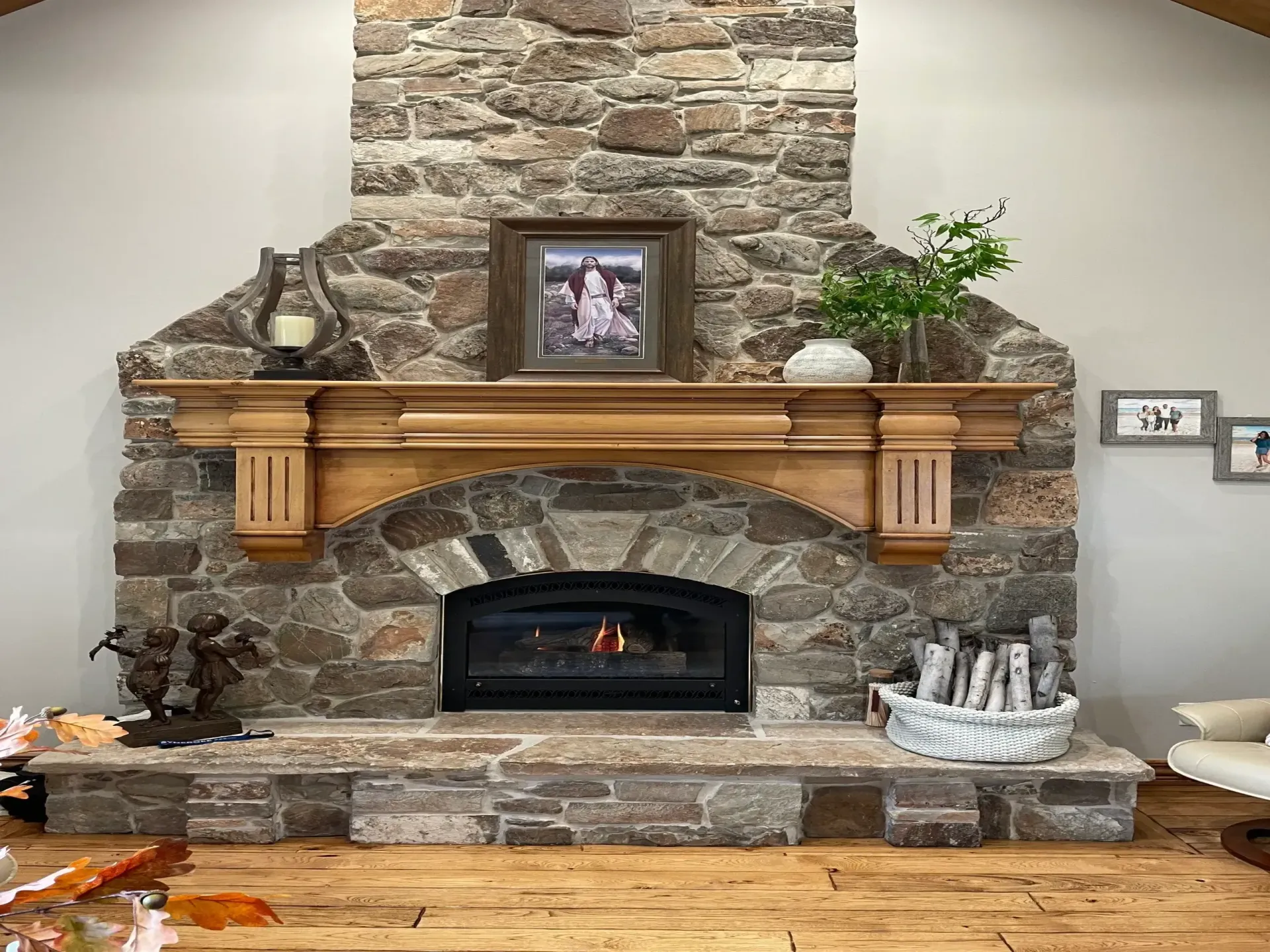 Stone fireplace with wooden mantel, framed photo, and decorative plants in a cozy living room.