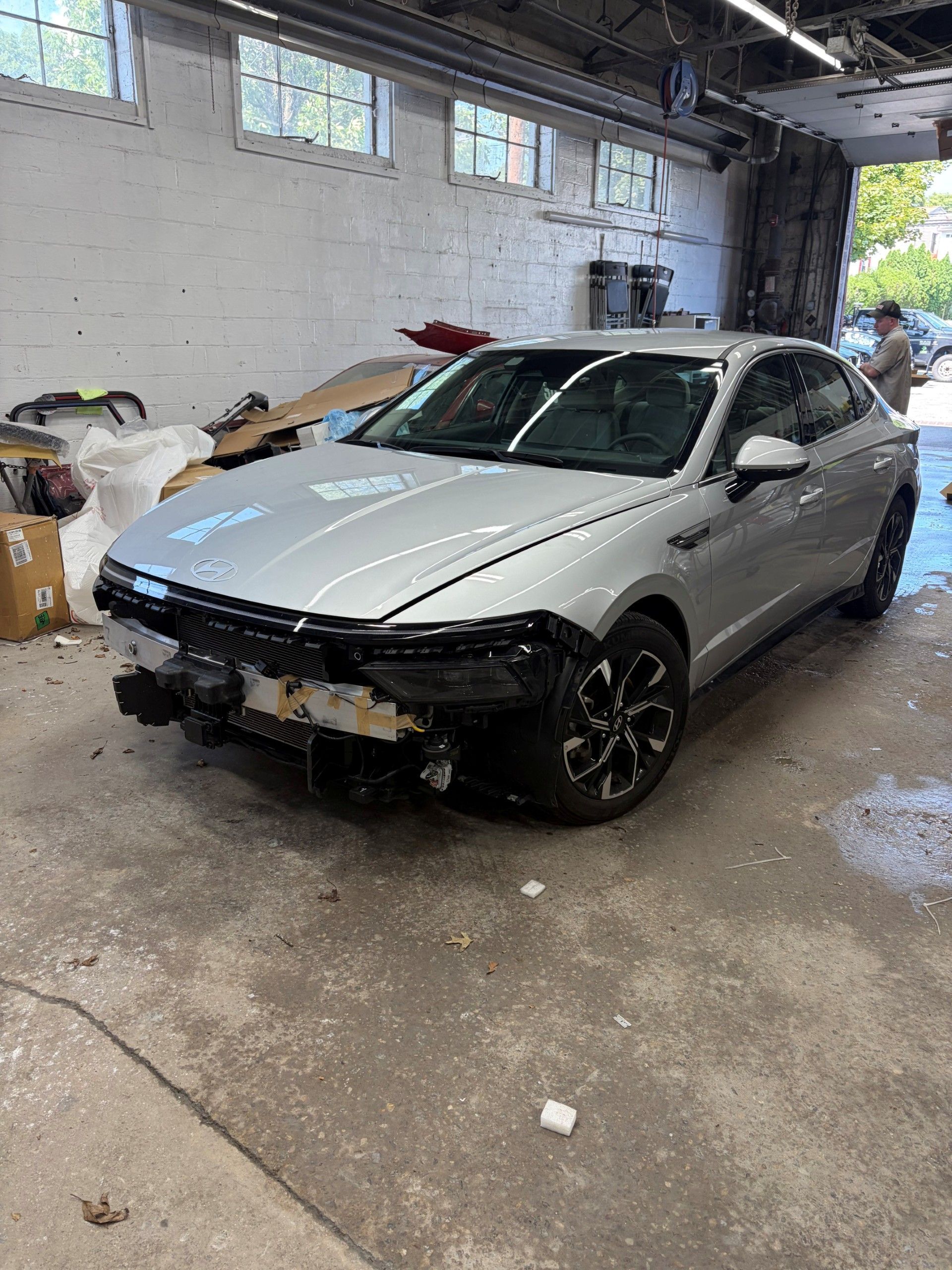 Worker sanding a car body in a bright auto repair shop