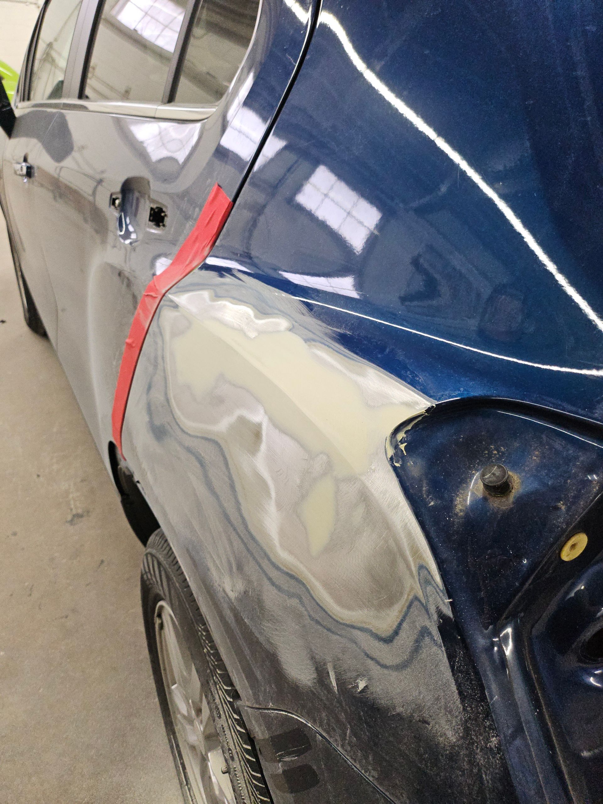 Damaged blue car side with scraped, dented rear quarter panel and exposed primer