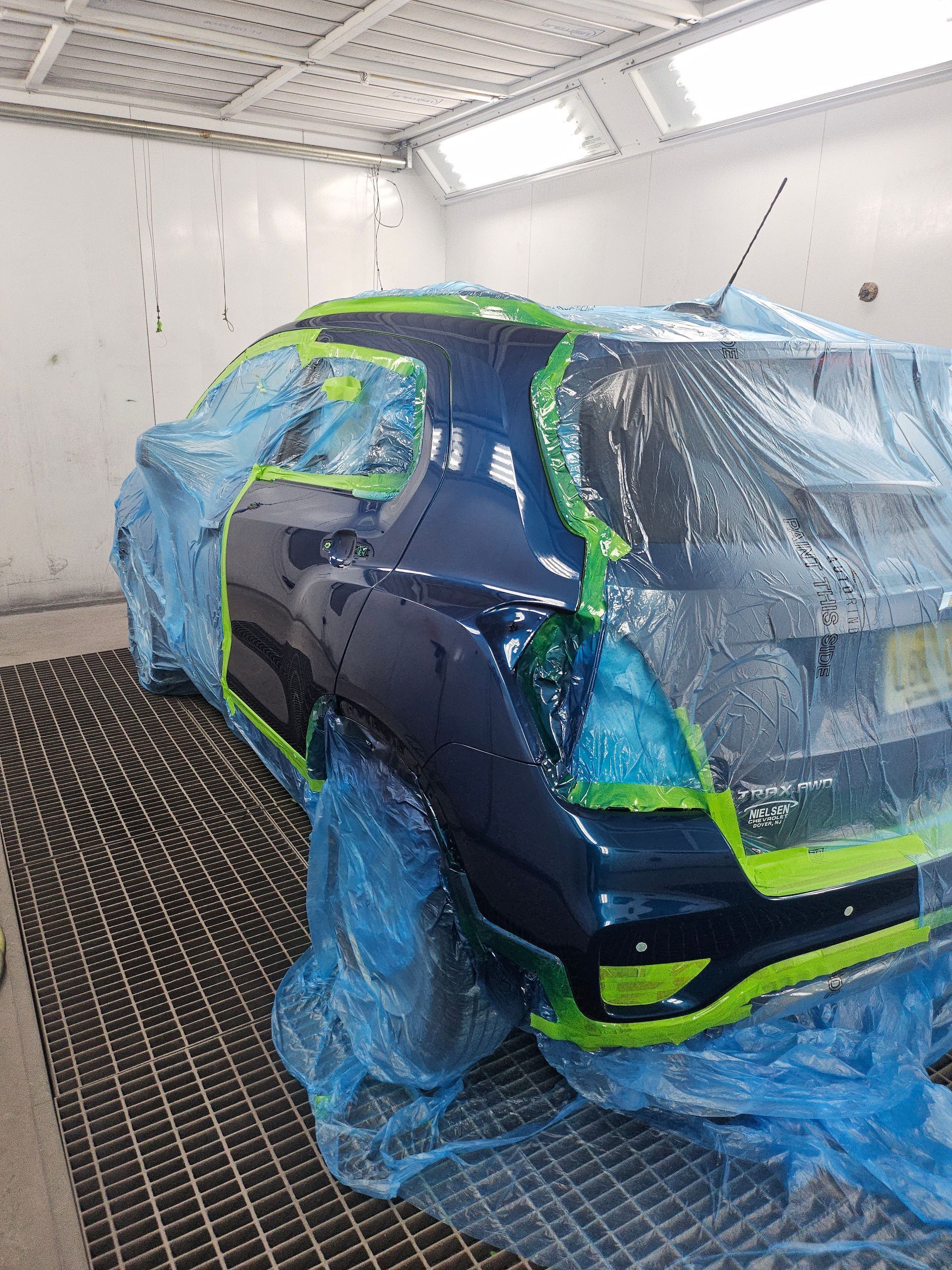 Car heavily masked with blue plastic and green tape in a white spray booth, ready for painting.