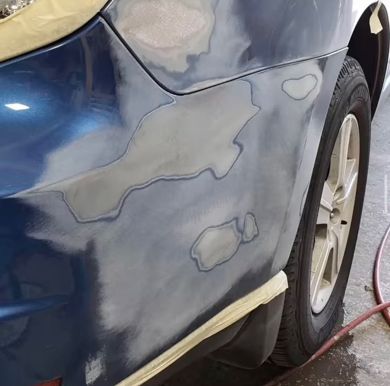 Blue car with sanded body panels and body filler patches, shown at a repair shop