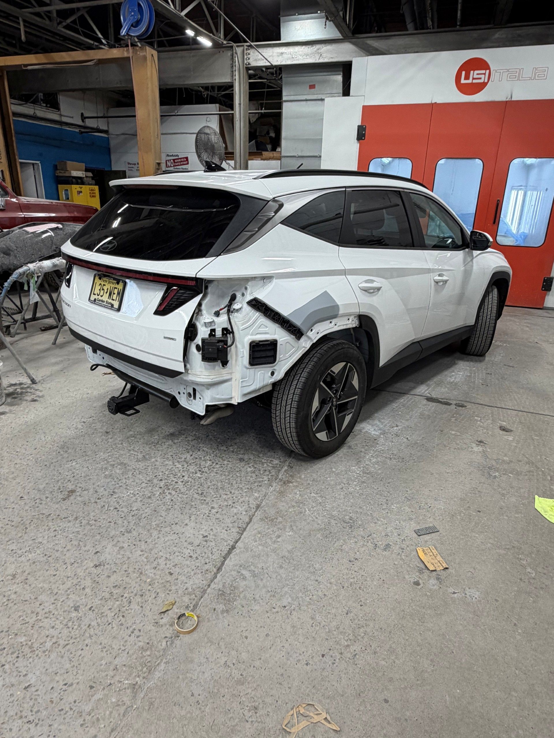 Mechanic working on a car in an auto garage, with another person in the background.