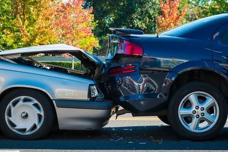 Two cars collided rear-end on a road, with visible damage to the blue car’s back and the silver car’s front.