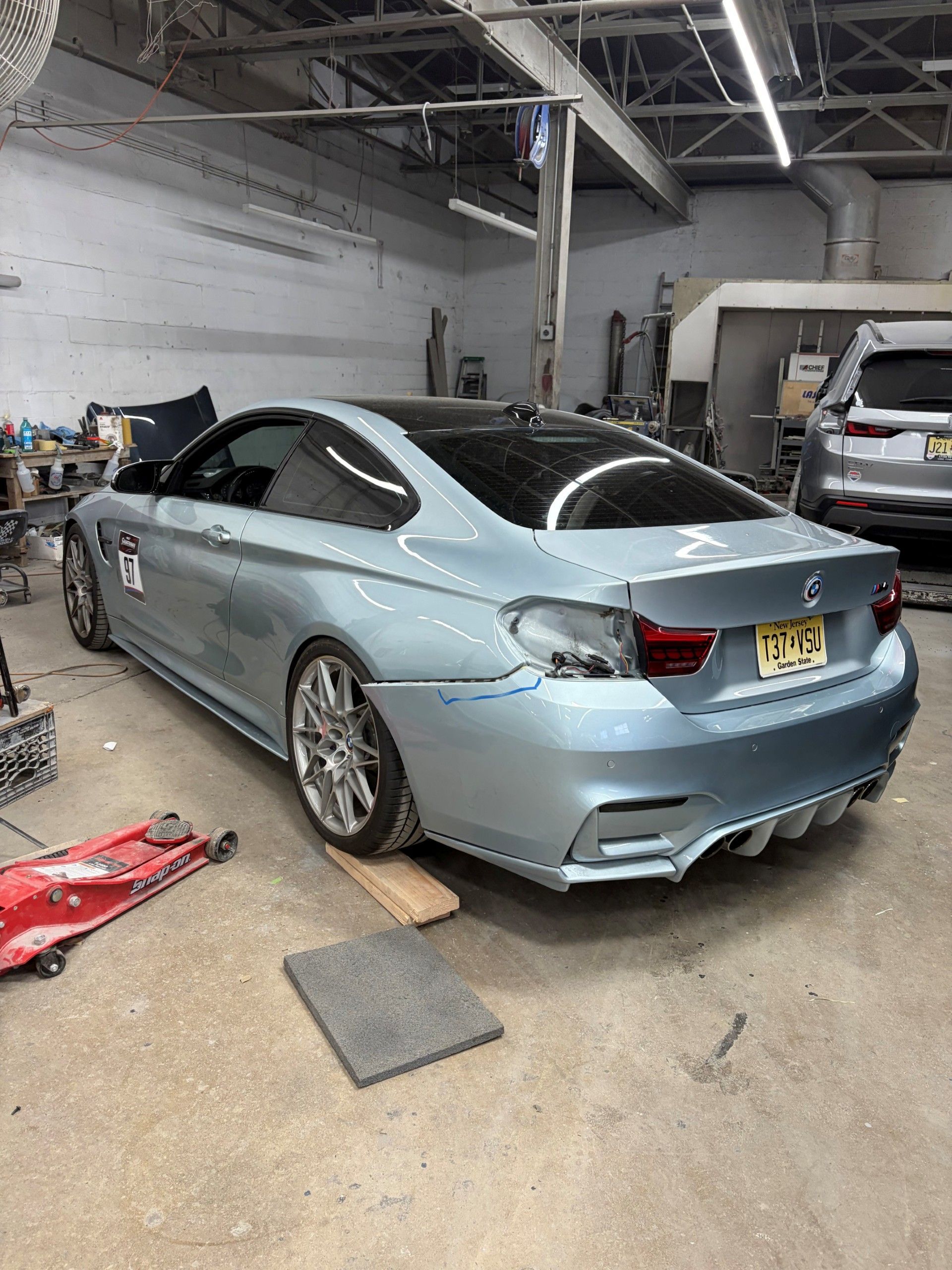 Mechanic sanding body filler on a blue car’s rear quarter panel in a repair shop