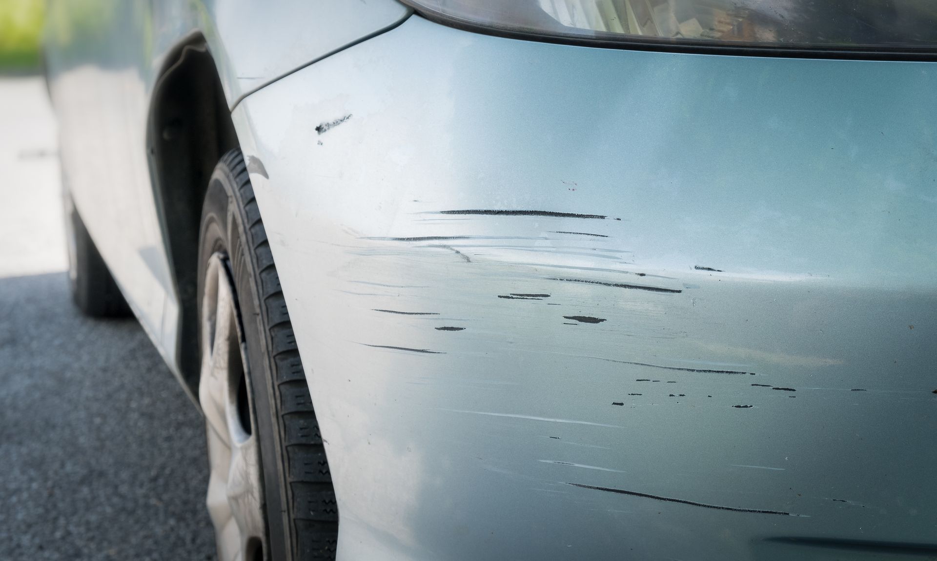 Close-up of a white car’s side panel with several scratches and scuff marks.