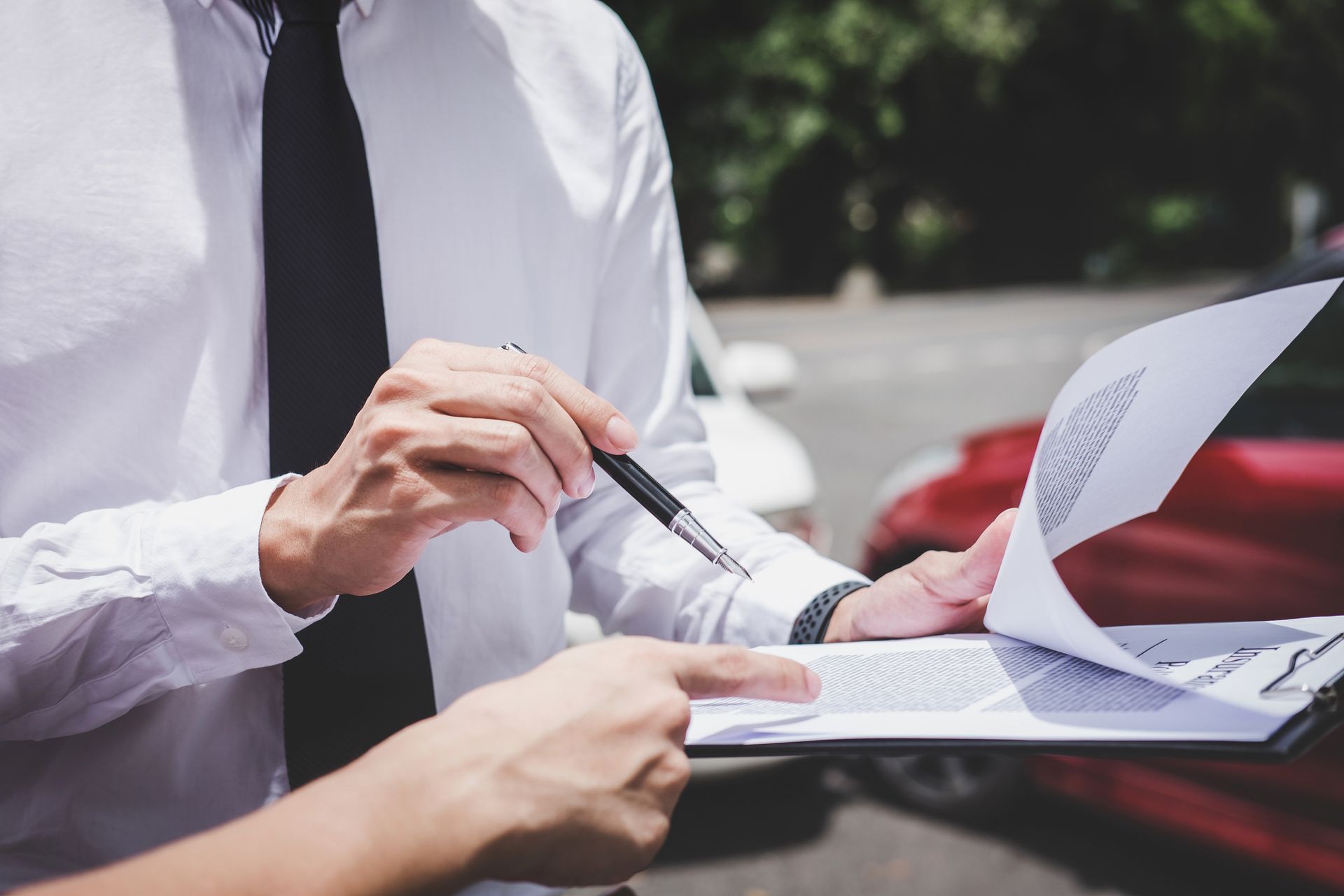 Person reviewing paperwork with a pen beside a red car outdoors