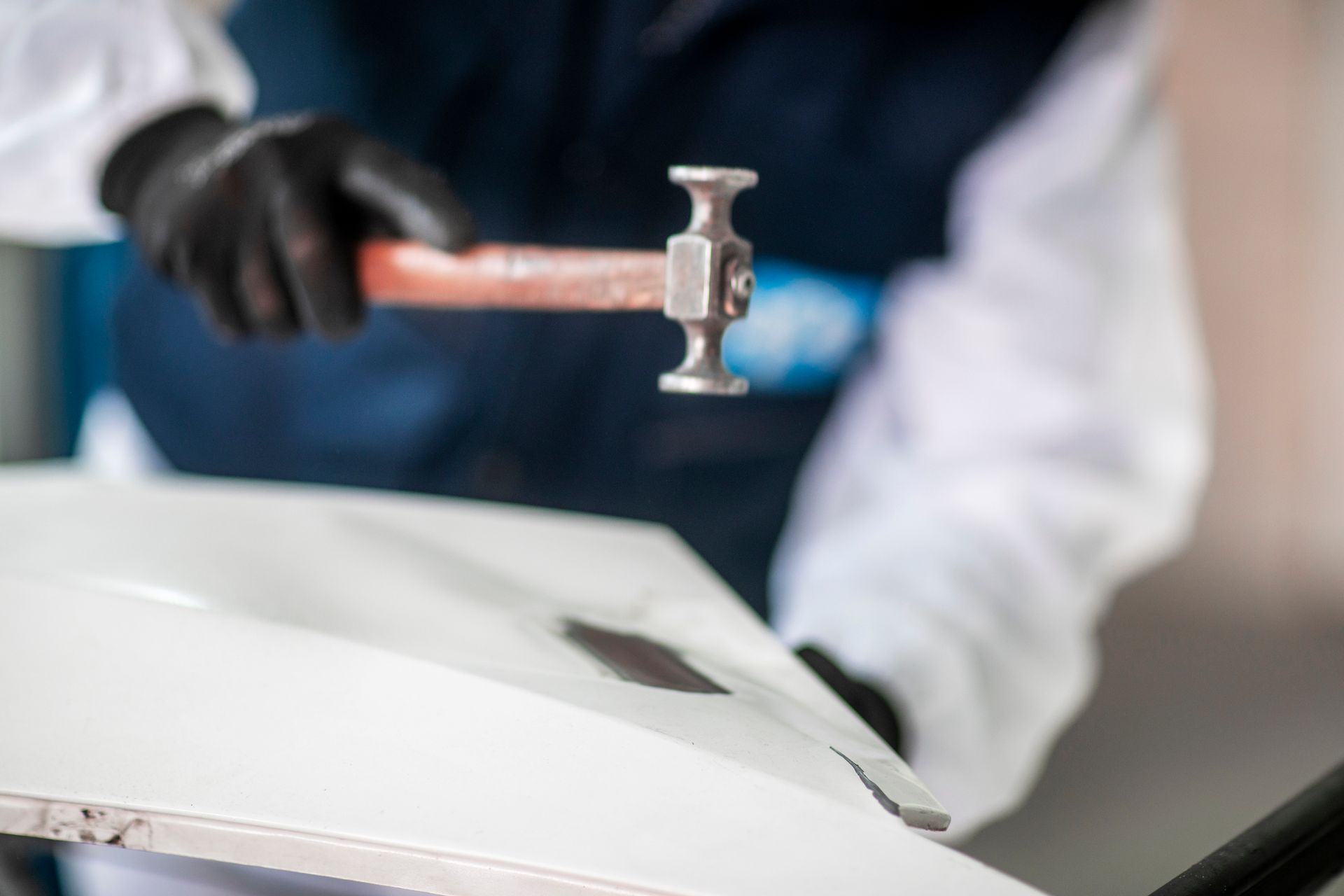 Gloved worker hammering a white car body in a repair shop