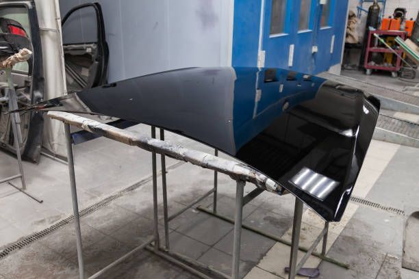 Black car hood panel resting on metal stands in an auto body workshop