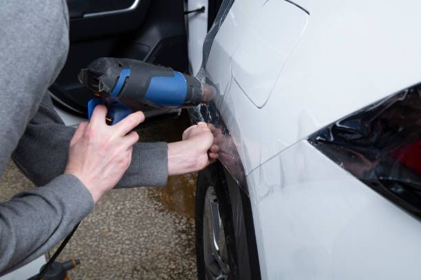 Person using a power drill to repair a white car’s side panel outdoors