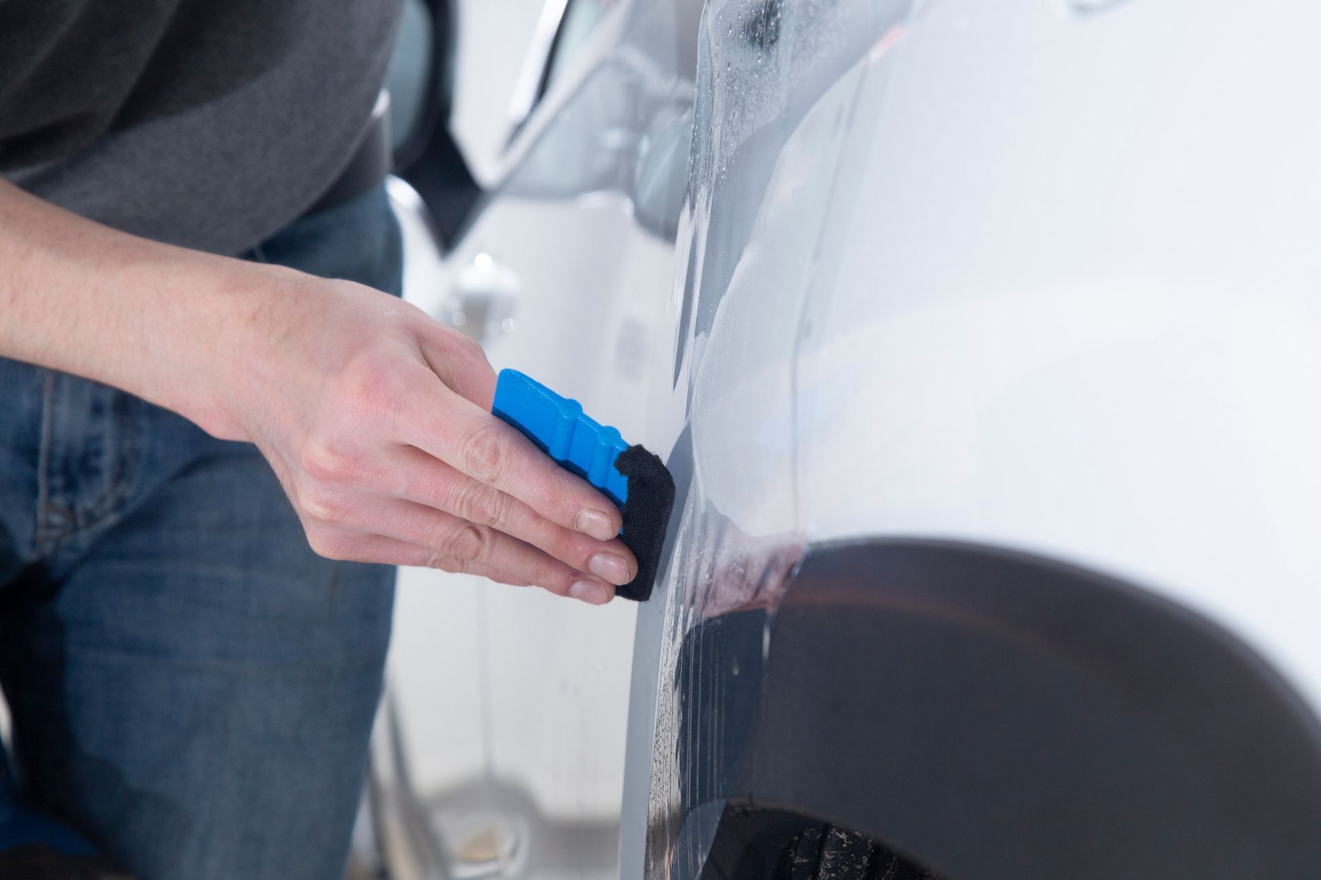 Hand wiping soap or wax onto a white car door with a blue applicator sponge