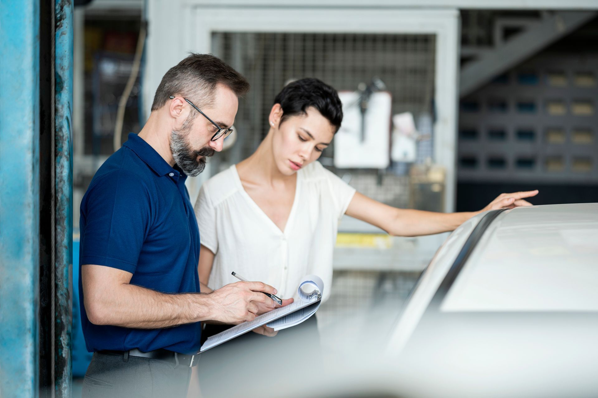 Two people reviewing documents beside a car in a bright garage