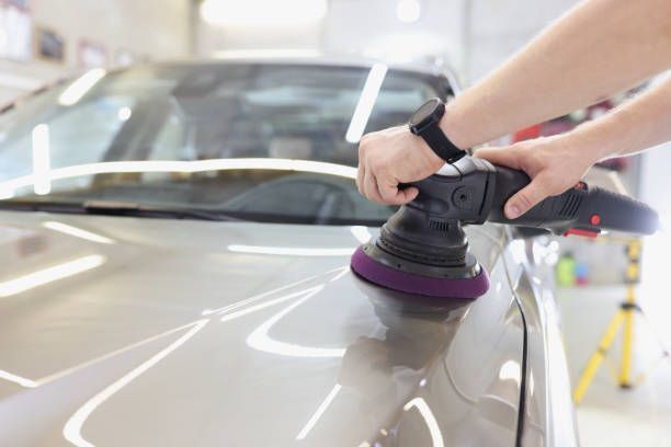 Hands polishing a car hood with a buffer in an auto detail shop