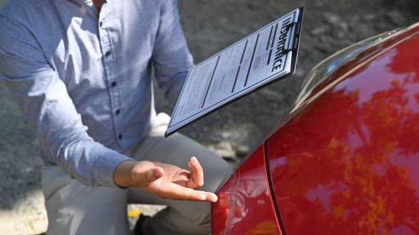 Person holding clipboard checks the side of a red car outdoors