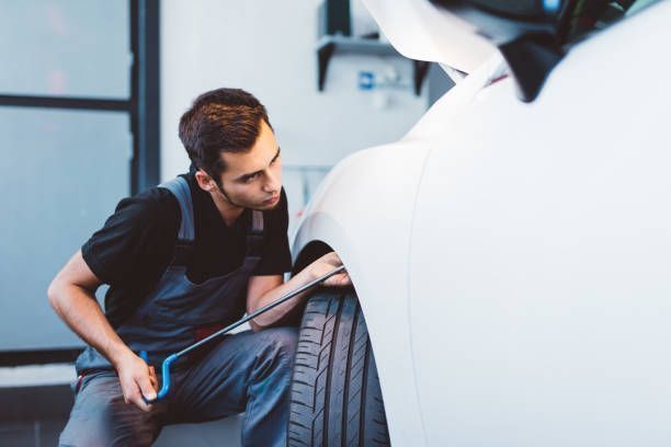 Technician in safety glasses and apron repairing a white car panel in a workshop