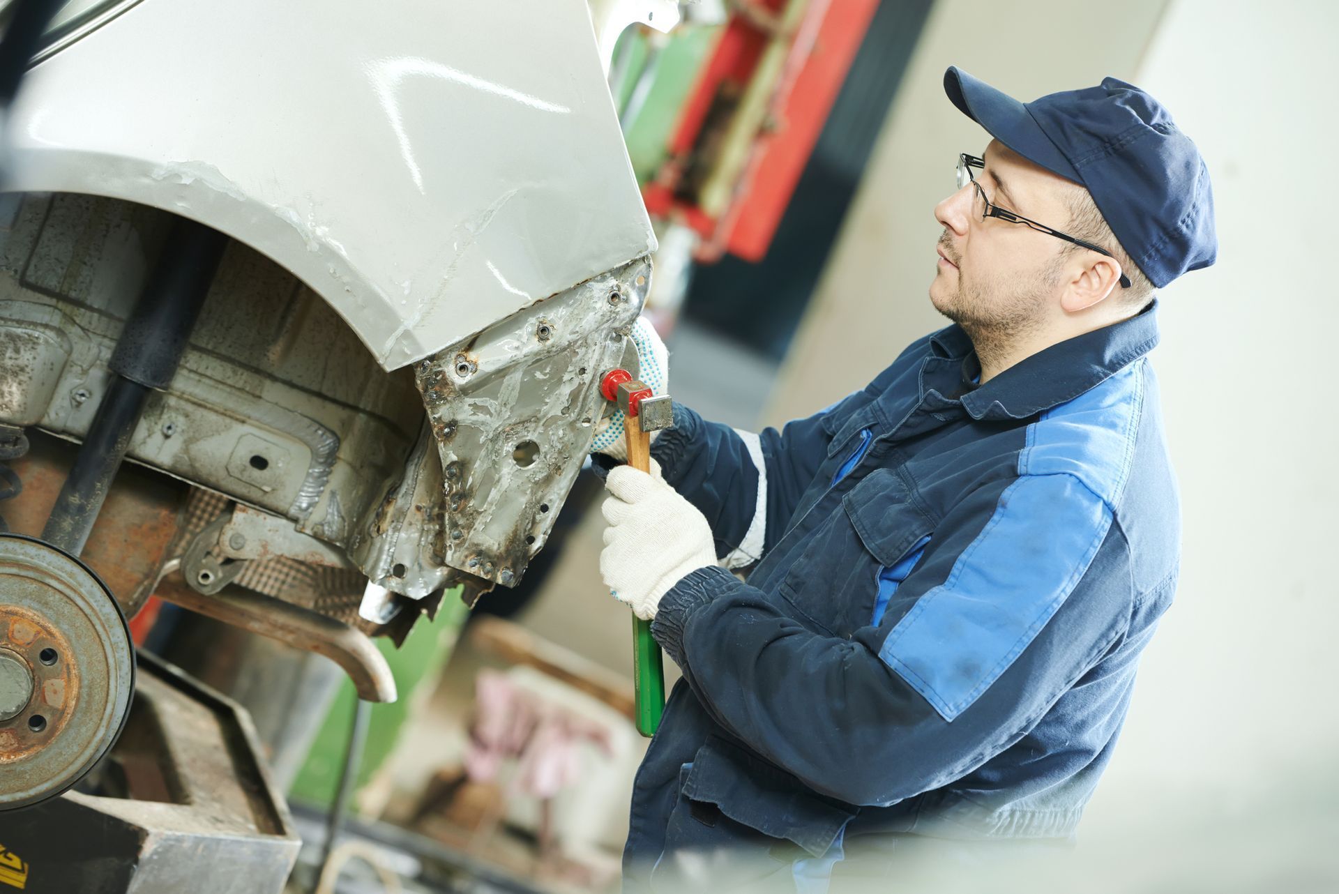 Mechanic in blue uniform using a tool to repair a car’s front wheel area in a garage