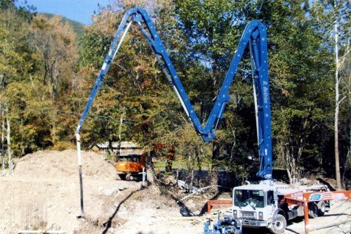 Concrete pump truck depositing concrete at a construction site near trees.