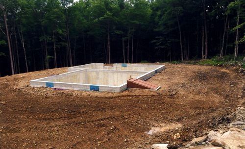 Concrete foundation in dirt clearing, surrounded by forest.