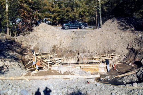 Construction site with a person working on wooden forms in a deep excavation; truck on the ground above.