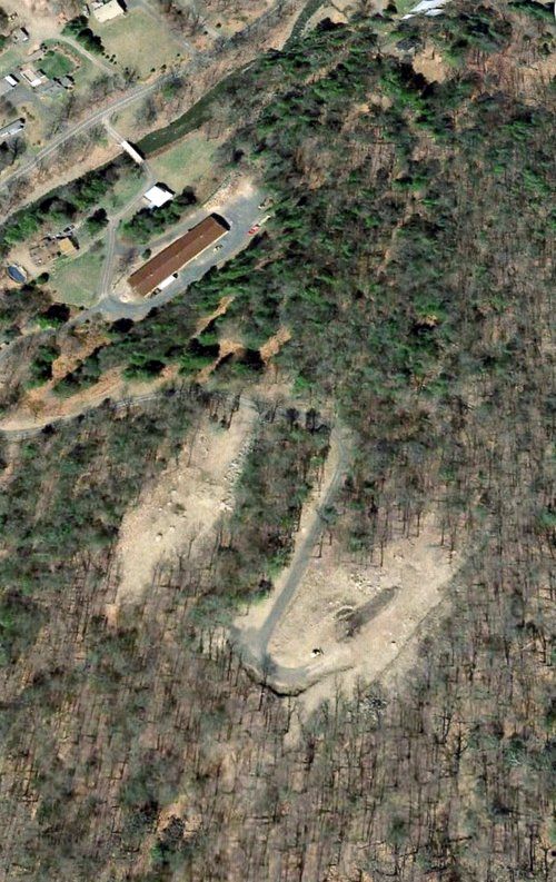 Overhead view of a mountain with a cleared section, road, and buildings near the top.