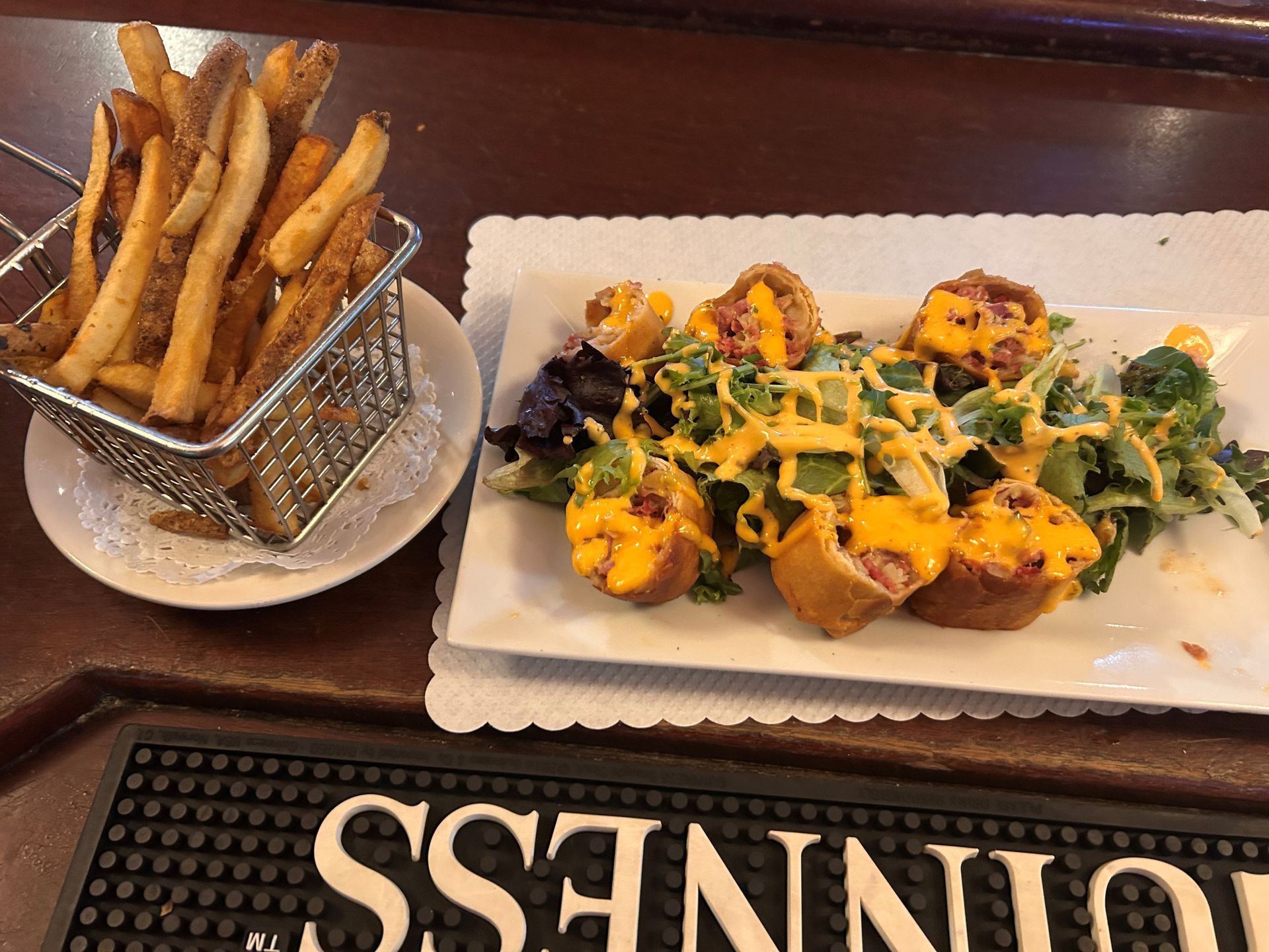 A plate of food next to a basket of french fries on a guinness bar mat