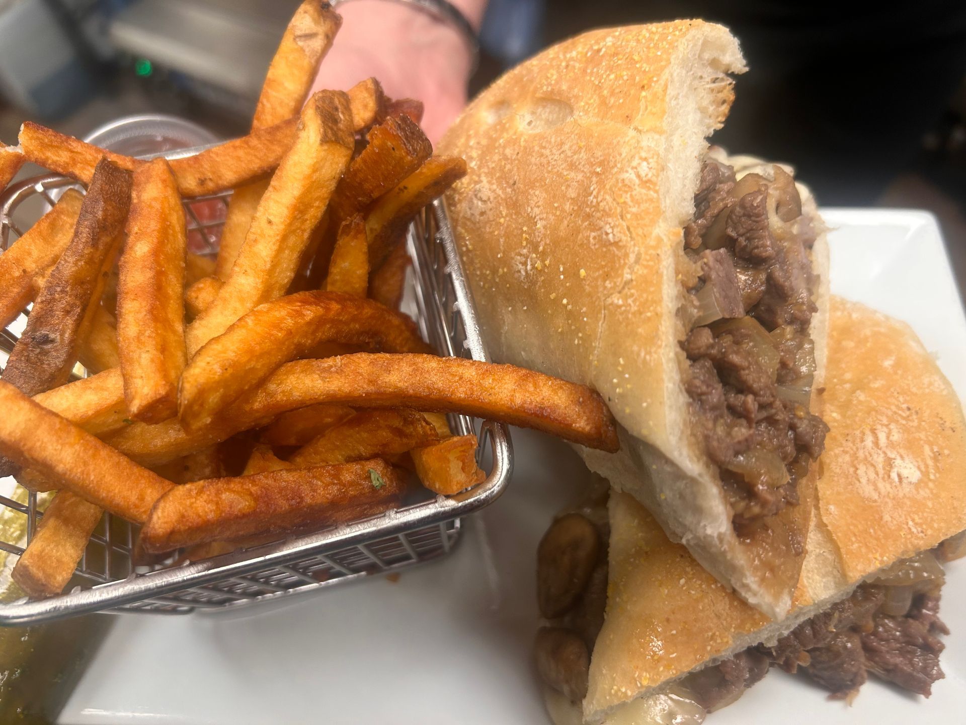 A steak sandwich and french fries are on a white plate.