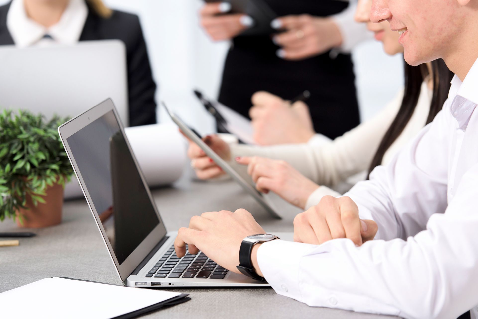 A group of people are sitting at a table using laptops and tablets.