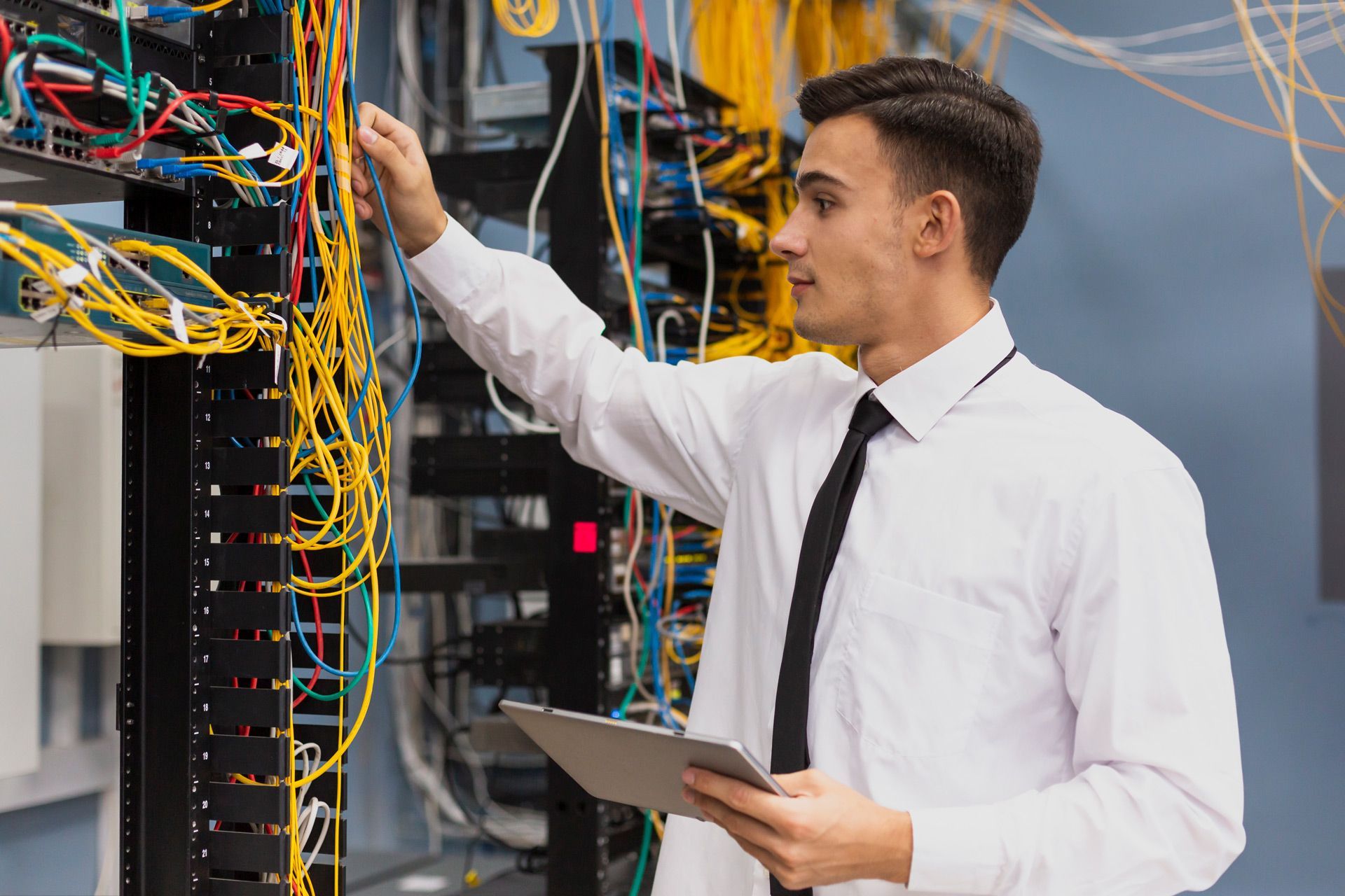 A man is working on a server in a data center while holding a tablet.