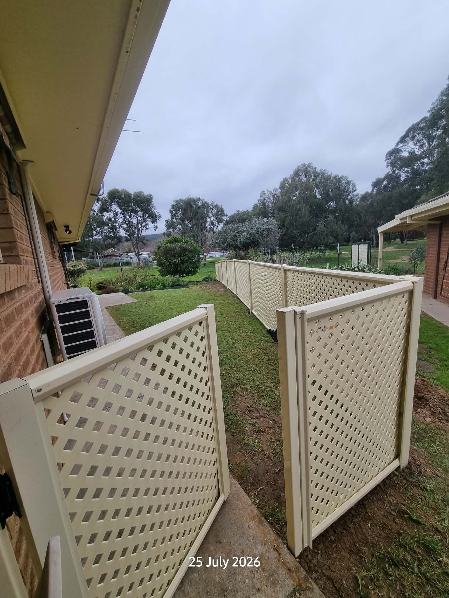 Backyard With Open Cream Lattice Gates, Grass Path, Brick House, and Trees Under Cloudy Sky — A Plus Project Maintenance in Wodonga, VIC