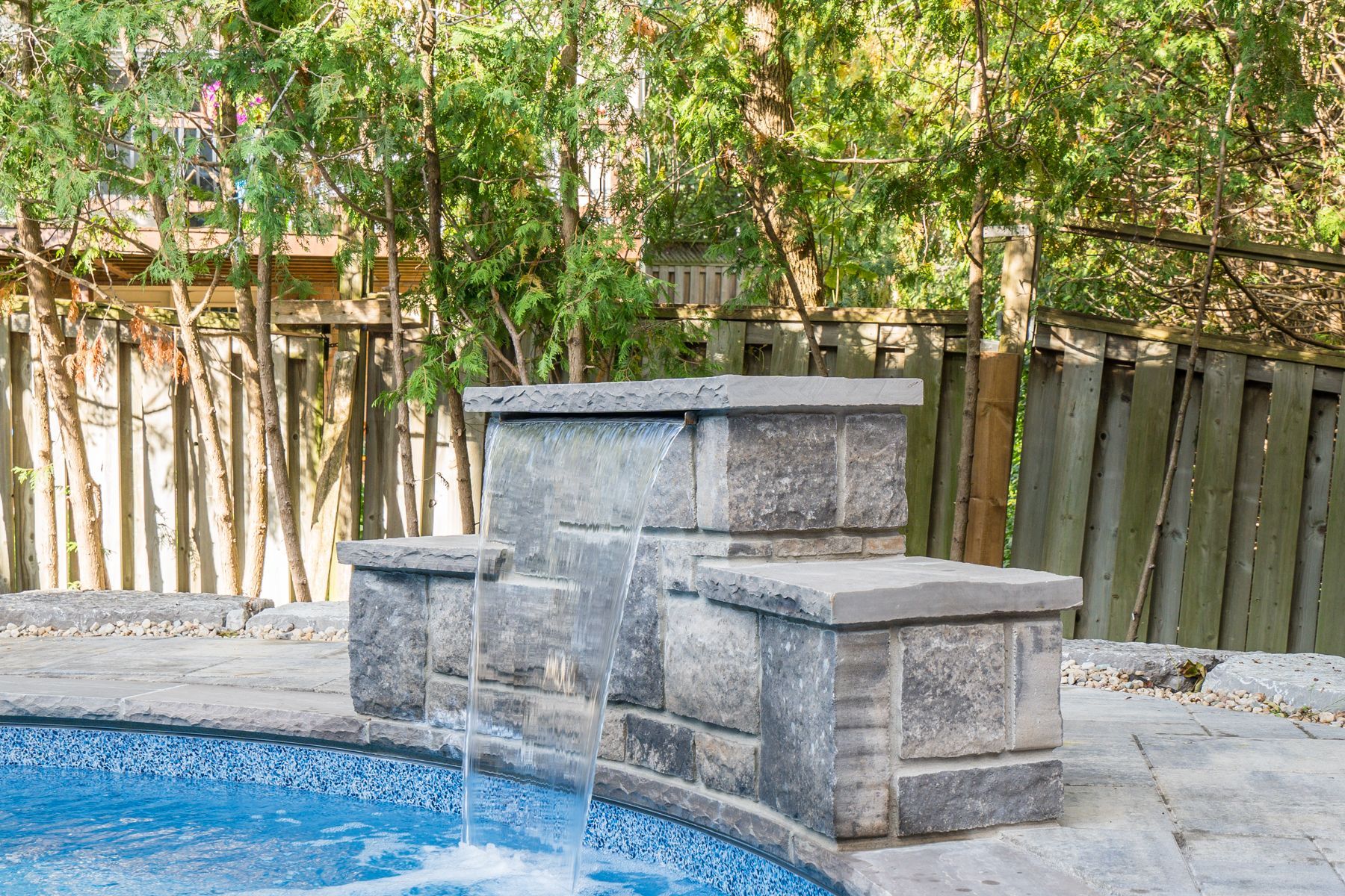 A swimming pool with a stone wall and a waterfall in the backyard.