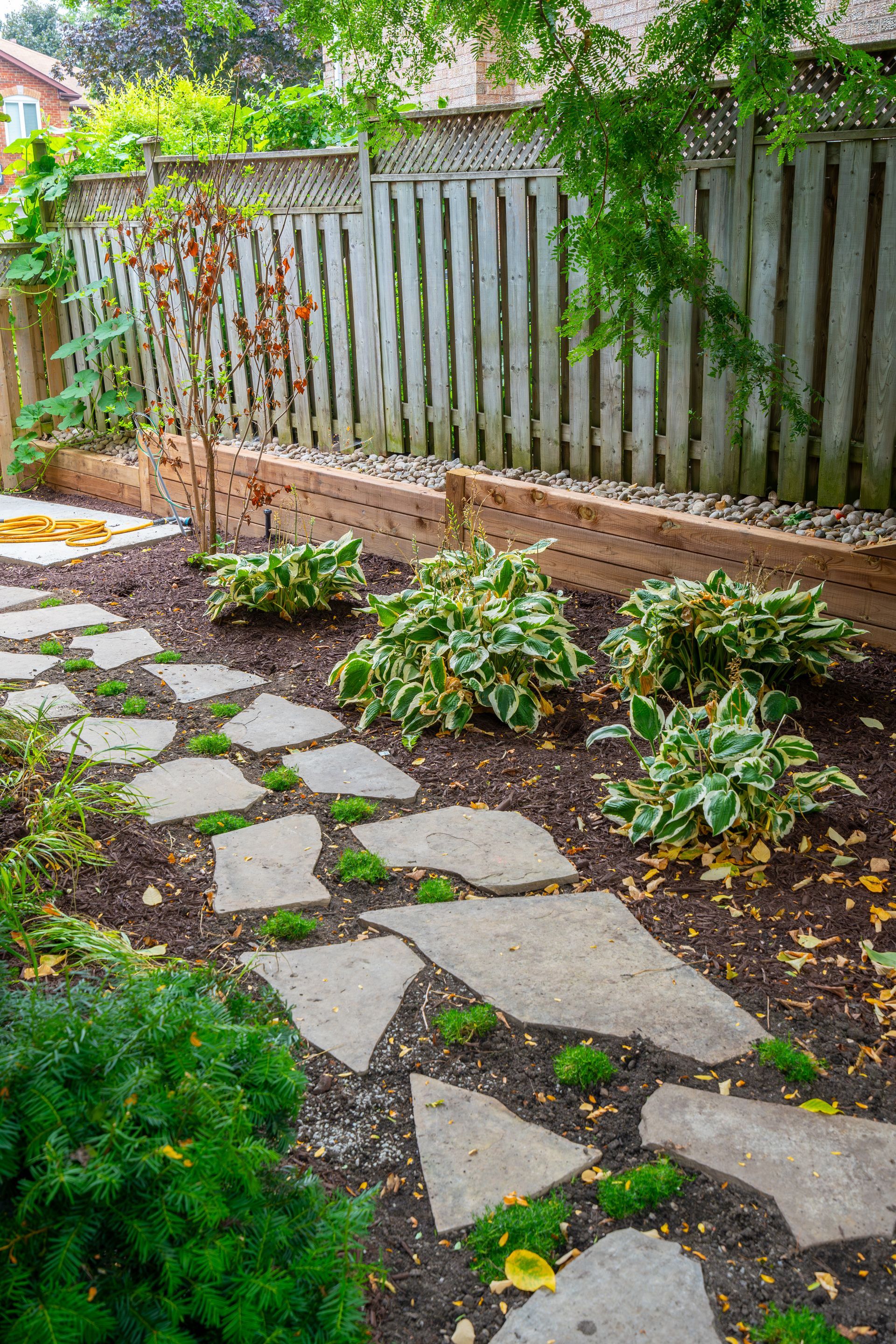 A stone walkway leading to a wooden fence in a backyard.