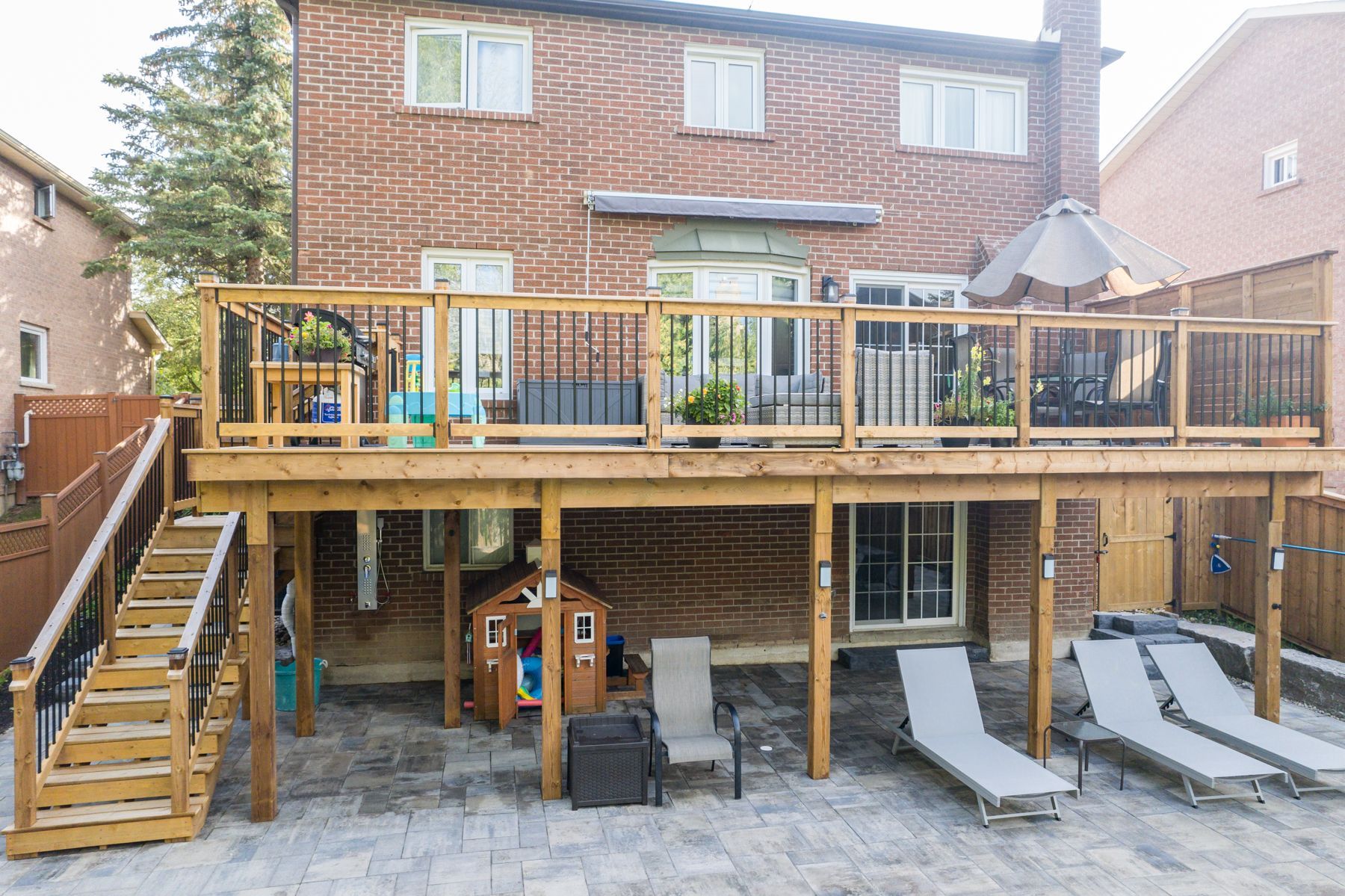 A large wooden deck with stairs leading up to it is in the backyard of a house.