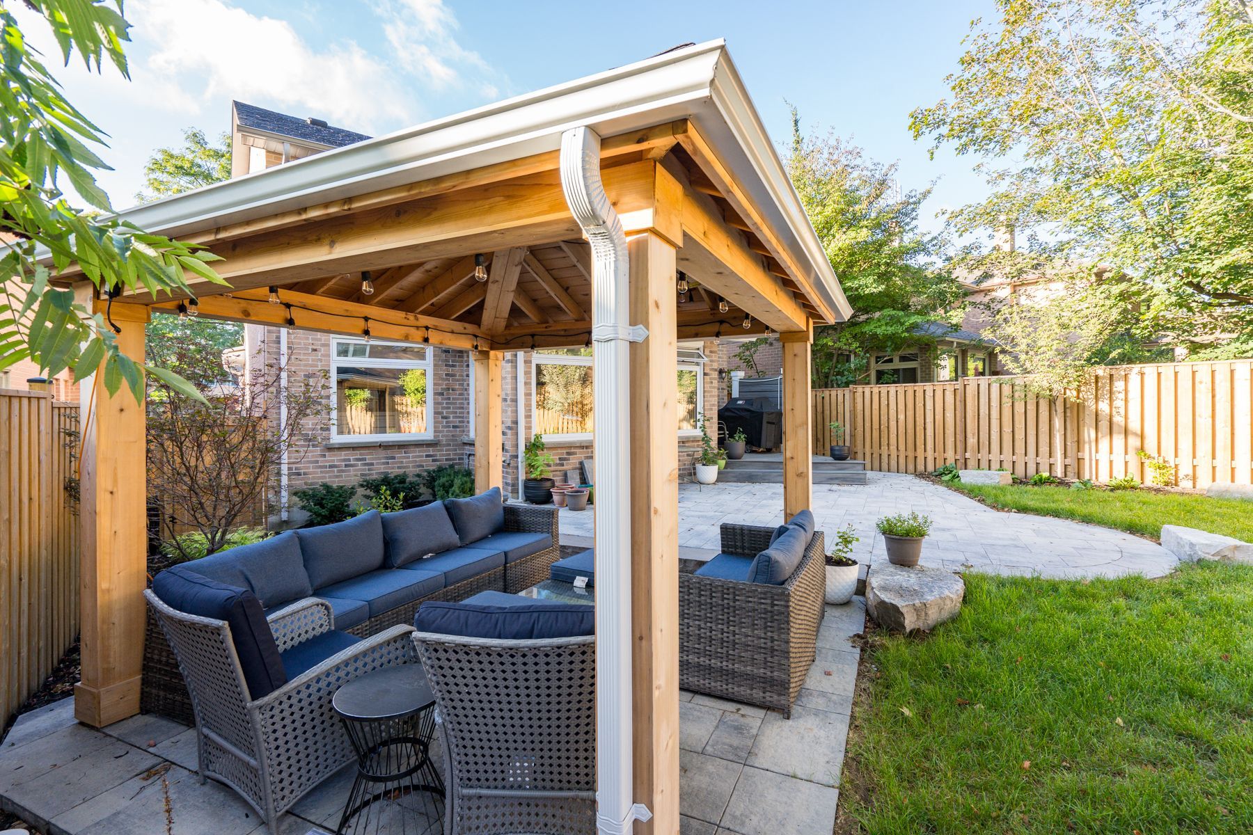 There is a gazebo in the backyard with a couch and chairs underneath it.