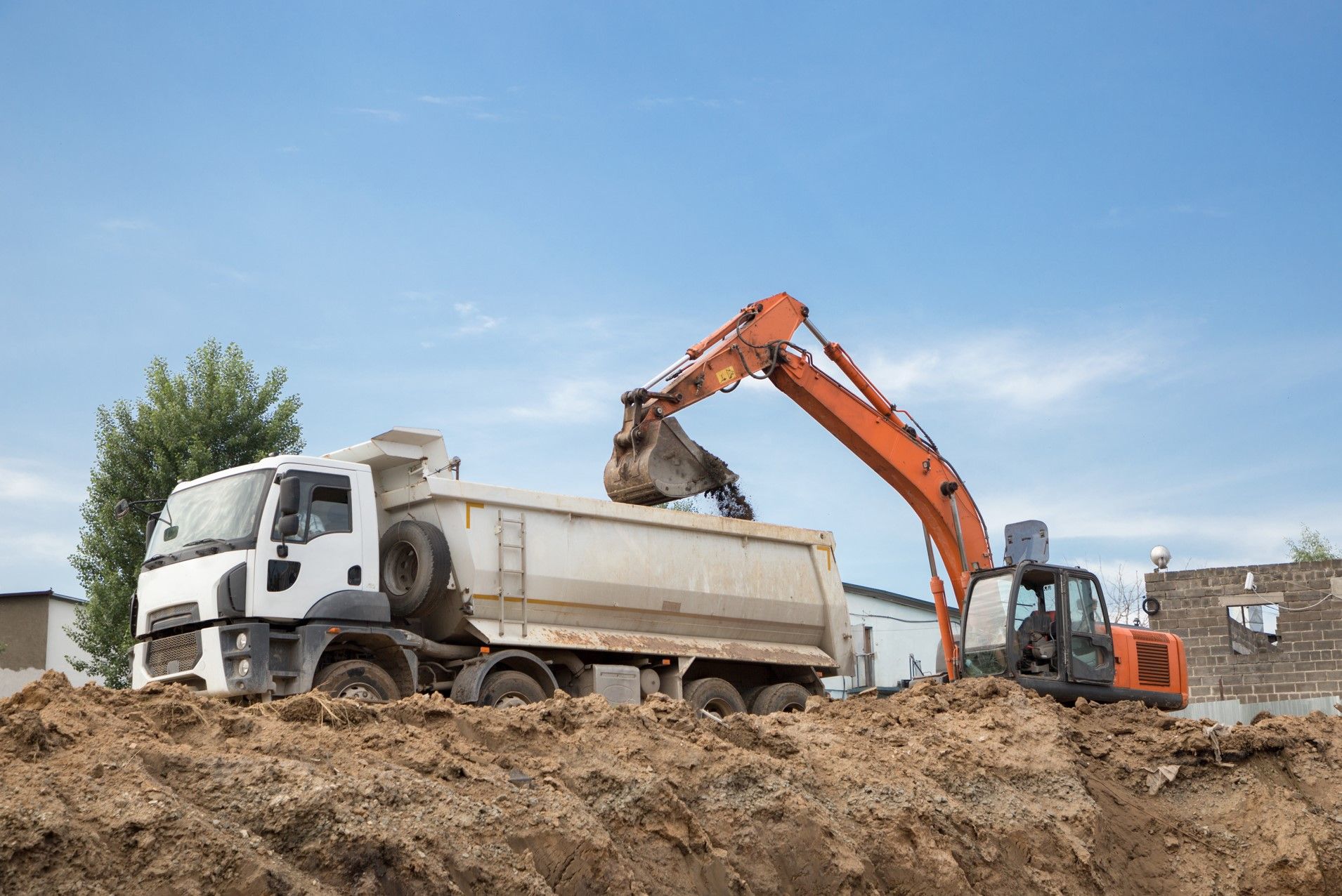 A dump truck is being loaded with dirt by an excavator.